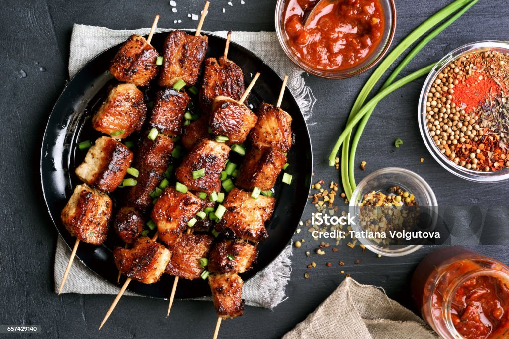 Bbq meat on wooden skewers on plate, top view